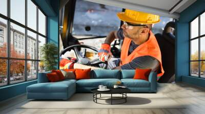 Construction worker operating heavy machinery at a job site during daytime wearing safety gear and focusing on the task Wall mural