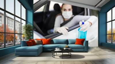 Portrait of woman with surgical mask sitting in car and holding sprayer sanitizer. Hygiene concept. Wall mural