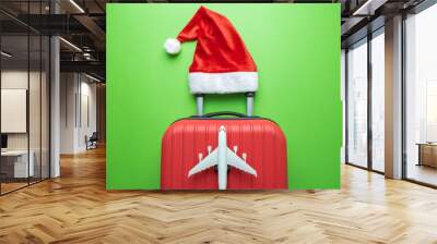 Suitcase with Santa hat and airplane model on green background minimal creative Christmas holiday travel concept. Wall mural