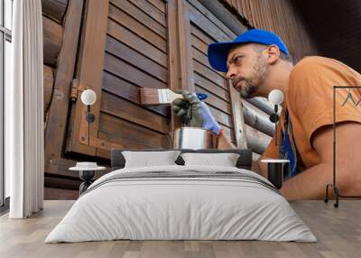 Worker applying protective varnish or wood oil on wooden house cottage exterior walls and window shutters Wall mural