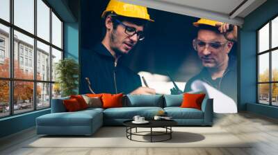 Scene of industrial workers wearing jump suit and yellow safety hat discussing the plan and operation while writing down the note on a clipboard,  Concept manufacturer quality control procedure. Wall mural