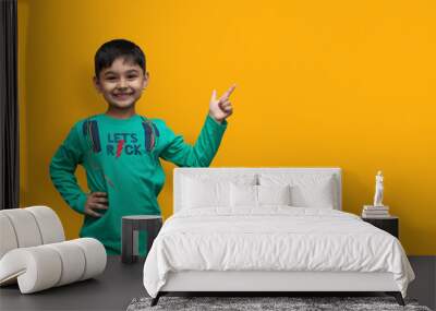 Happy young boy in shirt pointing up and holding arm white looking at the camera over isolated background and copy space Wall mural