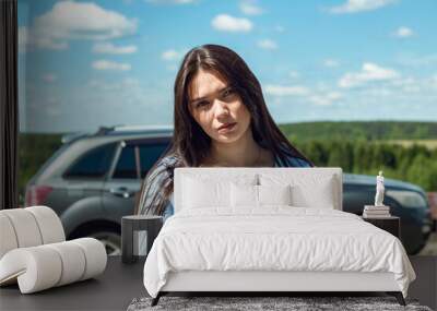 A girl stands by a car in the hot summer. Wall mural