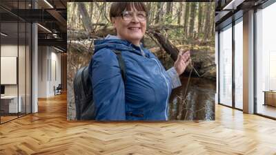 An elderly woman walks along a forest river. Wall mural