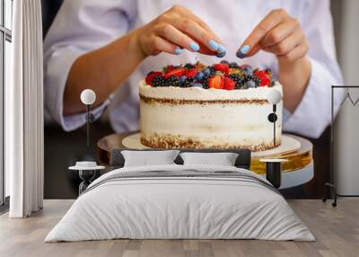 Girl chef cooks confectioner, decorates cake with forest berries. concept making without lactose cakes. Copy space, selective focus Wall mural