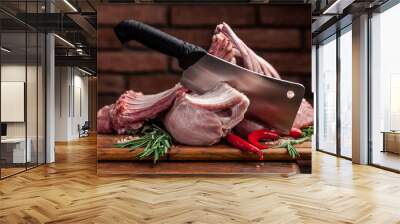 The concept of cooking meat. The man chef, the butcher, cuts raw meat with beef, lamb, veal, holding a knife in his hand, on a wooden table, next to lie raw vegetables, cherry, parsley, dill. Wall mural