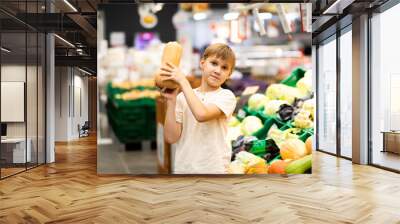 Kid teenager shopping for fresh organic fruits and vegetables in supermarket. Cute boy holding pumpkin in a hands. Wall mural