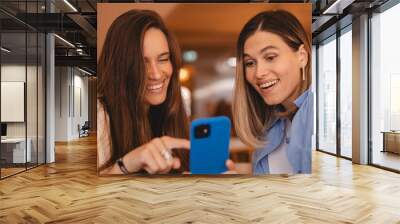 Portrait of excited impressed two  women sisters friends fellows use devices recommend select choose decide discount options, point finger on phone, screaming wow, open mouth, omg, sitting in cafe. Wall mural