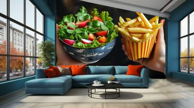 Hand holding a bowl of fresh salad and another hand with crispy fries, highlighting the contrast between healthy and fast food choices. Wall mural