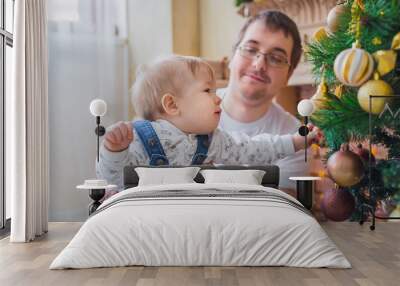 Portrait of happy young father and baby son playing together in bright room with Christmas interior at home. Family, holiday, parenthood, playing, game, childhood and leisure time concept Wall mural