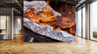 Process of cooking fresh meat steaks, sausages and potatoes in foil on brazier at summer local food market - close up view. Outdoor cooking, gastronomy, cookery, street food concept Wall mural