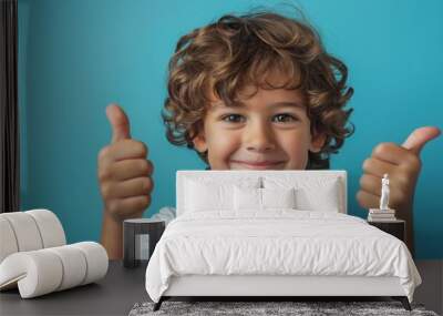 Smiling young boy giving two thumbs up against a blue background. Concept of positive attitude, happiness, and approval. Wall mural