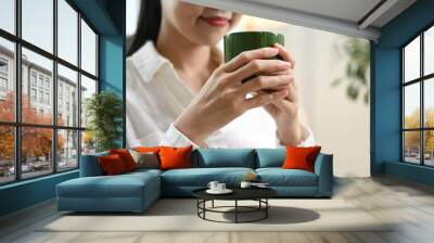 A woman is sitting on the floor with a green mug in her hand. Wall mural