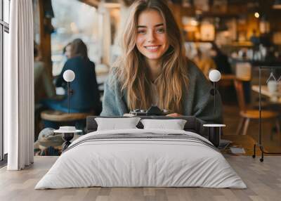 A young woman sits at a wooden table in a cozy cafe, holding a camera in one hand. Generative AI Wall mural