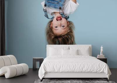 beautiful little girl hanging upside down on blue background Wall mural