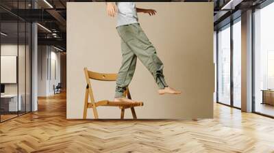 Cool indian boy balancing on one leg on a wooden folding chair in a beige room Wall mural