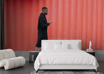 Side view of sulky black man in a warm coat walking in front of corrugated wall Wall mural