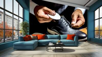 A man carefully uses a cloth to polish his shoes, highlighting attention to detail in his grooming routine. Wall mural