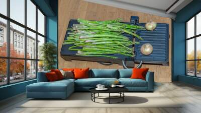 Kitchen griddle with a large bunch of tender green asparagus and two onions Wall mural