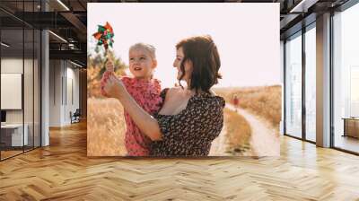 Mom shows little daughter how to use a windmill on outdoor. ESG and Clean Energy Concept. Wall mural