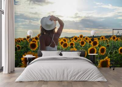 a young tanned girl in a white dress and hat walks in a field at sunset Wall mural