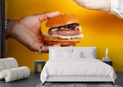 Hands holding burger against yellow background. Fast food, junk food concept. Wall mural