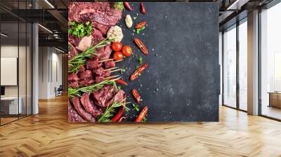 FreVarious fresh meat-portioned steaks, beef tenderloin, shin steaks, meat on skewers lie on a dark background. The meat is decorated with seasonings, vegetables and herbs. Top view, free space for te Wall mural