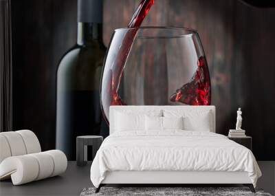 Red wine is poured into a glass from a bottle on a blurred wooden background, a stream of red wine from the bottle swirls in the glass, close-up. Free space for text. Wall mural