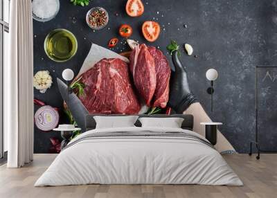 The butcher shows a section of fresh meat tenderloin, which lies on parchment on a dark background. On the table-seasonings, spices, vegetables and herbs. Top view, free space for text. Wall mural