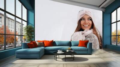 A girl in a sweater and mittens in winter stands on a snow-covered background Wall mural