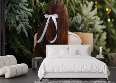 A girl with long hair stands with her back in a winter forest with a bouquet of fir branches. Snowy winter Wall mural