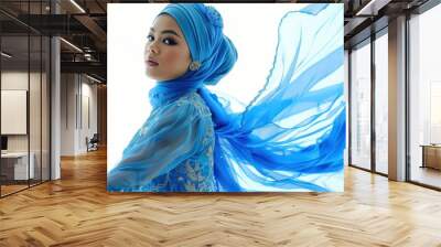 Portrait of a beautiful Asian female model dressed in a blue dress and hijab, standing out against a white background Wall mural