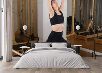 Young girl doing Pilates barre in a gym. Beautiful slim woman in black clothes performs exercises to strengthen the spine and back muscles Wall mural