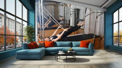 Young girl doing Pilates on trapeze table in the gym. Beautiful slim woman in black clothes performs exercises to strengthen the spine and back muscles Wall mural