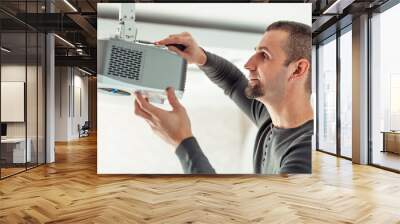 A man independently installs a multimedia video projector for a home theater or presentations on the ceiling. Wall mural