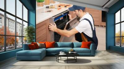 A man or service worker in special clothing installs, disassembles or performs maintenance of a dishwasher built into the kitchen furniture Wall mural