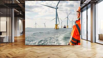 A worker in reflective gear looks at wind turbines at sea, symbolizing the use of renewable energy and sustainable practices. Wall mural