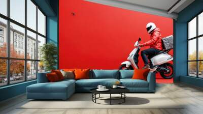 Delivery man riding scooter with thermal backpack wearing red jacket on red background Wall mural