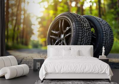 Two new all season tires with alloy wheel rims lying on road in a forest Wall mural