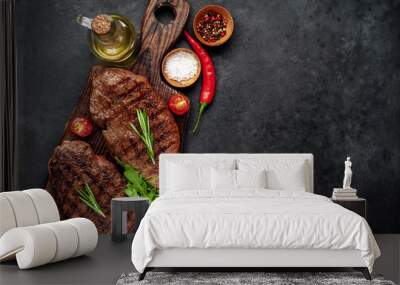 Two grilled beef steaks with spices and herbs on a cutting board on a stone background with copy space for your text Wall mural