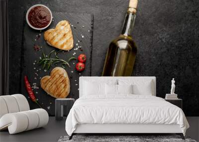 
two heart shaped grilled chicken breast steaks with spices, a bottle of white wine for Valentine's Day dinner on a stone background with copy space Wall mural