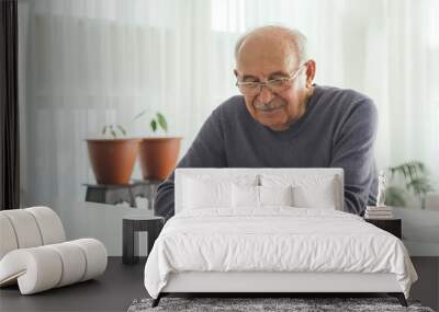 Retired man using computer technologies at home. Wall mural