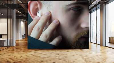 Close-up portrait of a young bearded guy of twenty-five years old, looking at the camera, in wireless white headphones in his ears. Studio advertising photo of headphones. Athlete in headphones Wall mural