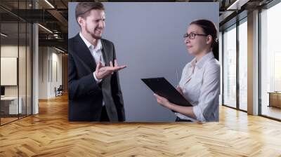 portrait of young business people in business clothes. The guy is outraged about the report of a business girl with a folder for documents. Studio photo on a gray background. Wall mural