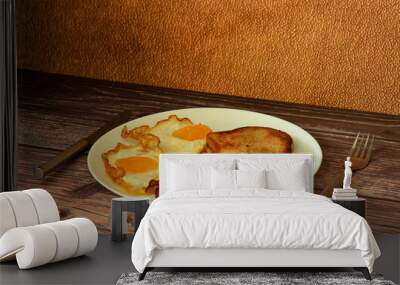 A plate of hearty and nutritious breakfast, scrambled eggs, scrambled bacon and toasted bread on a dark wooden table, with cutlery nearby. Wall mural