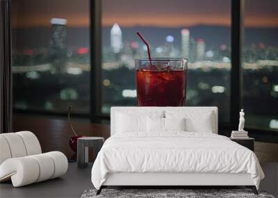 Close-up of a glass with a red-orange sweet and sour cocktail, ice cubes, on the windowsill with a beautiful view from the window of a skyscraper to the night city. Wall mural