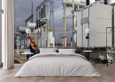 An electrical engineer inspects power transformers in power plants. An engineer in a red helmet and protective overalls. Substation work Wall mural