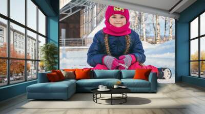 A girl child in winter clothes sits on a snowy path in the winter. Walk in winter Wall mural