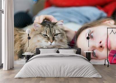 young girl is lying on the sofa with a cat looking at the camera. pet, love for animals Wall mural