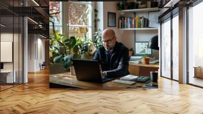 Man working on a laptop in a home office surrounded by plants with sunlight coming through the window Wall mural